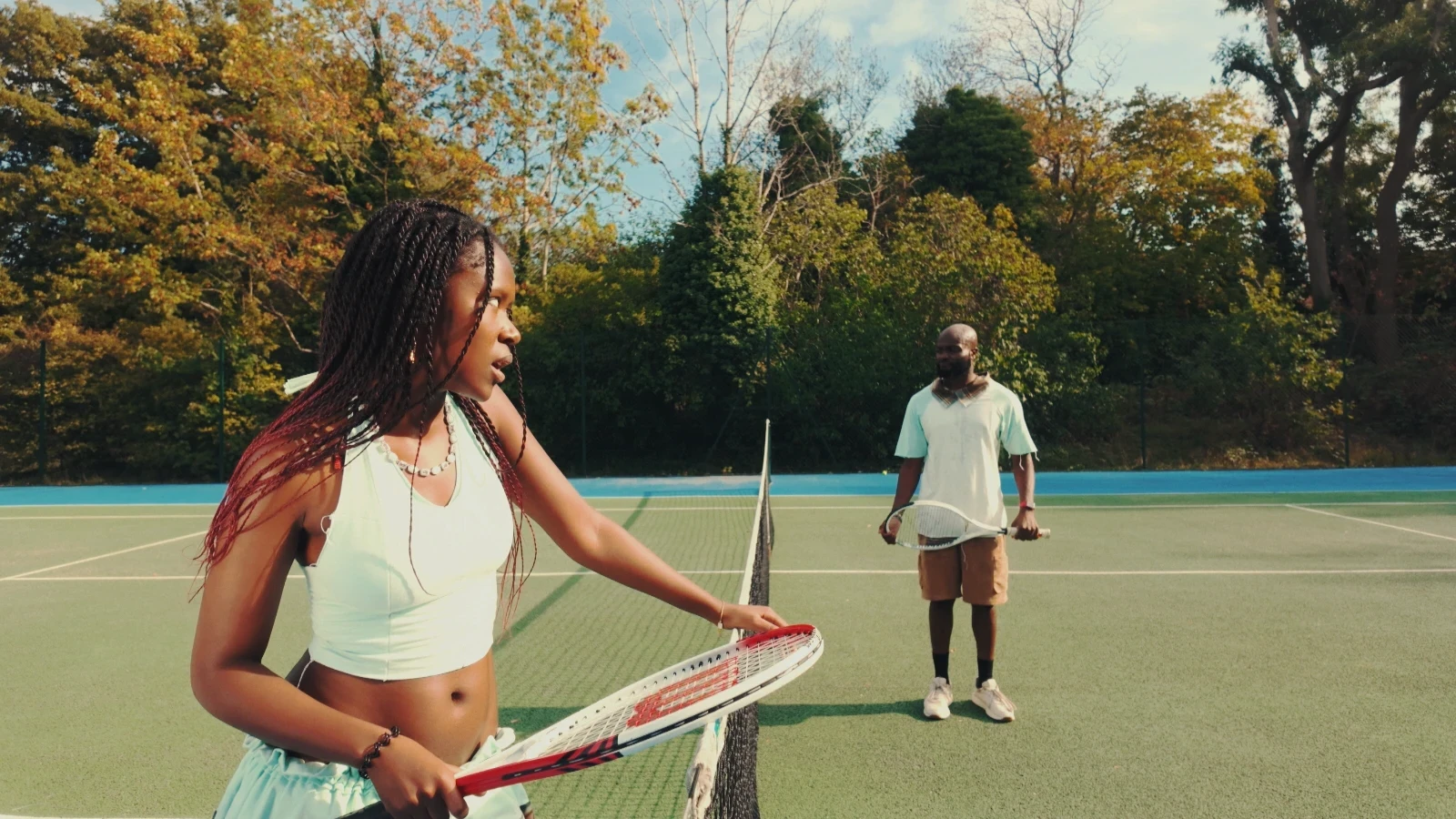 Kah'Nya at the net, racket in hand, with obi on the far side of the court