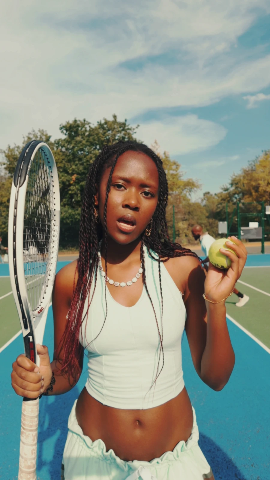 Kah'Nya holding her racket upright and a tennis ball, with obi walking behind her